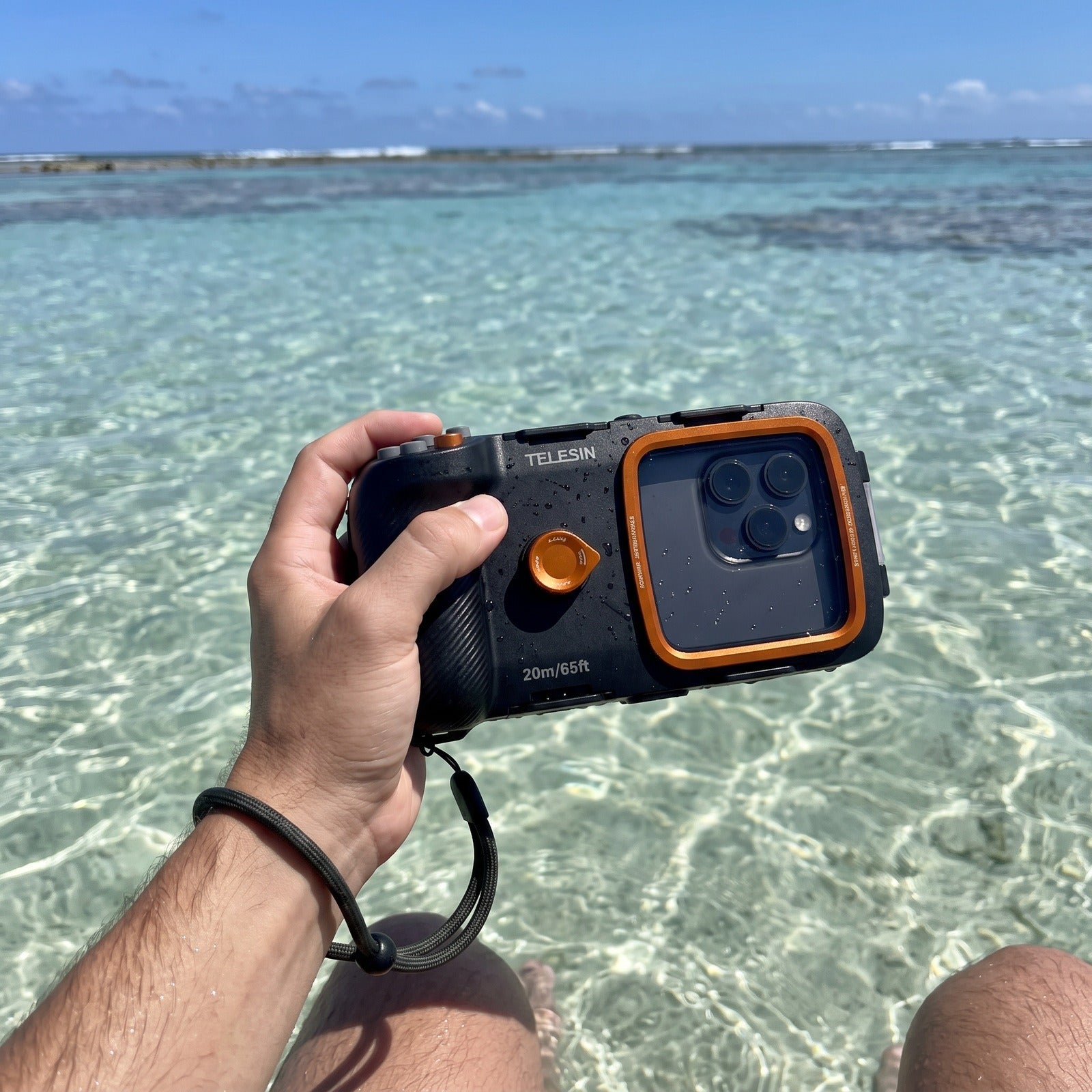 Hand holding the Tideglass housing beside a clear lagoon