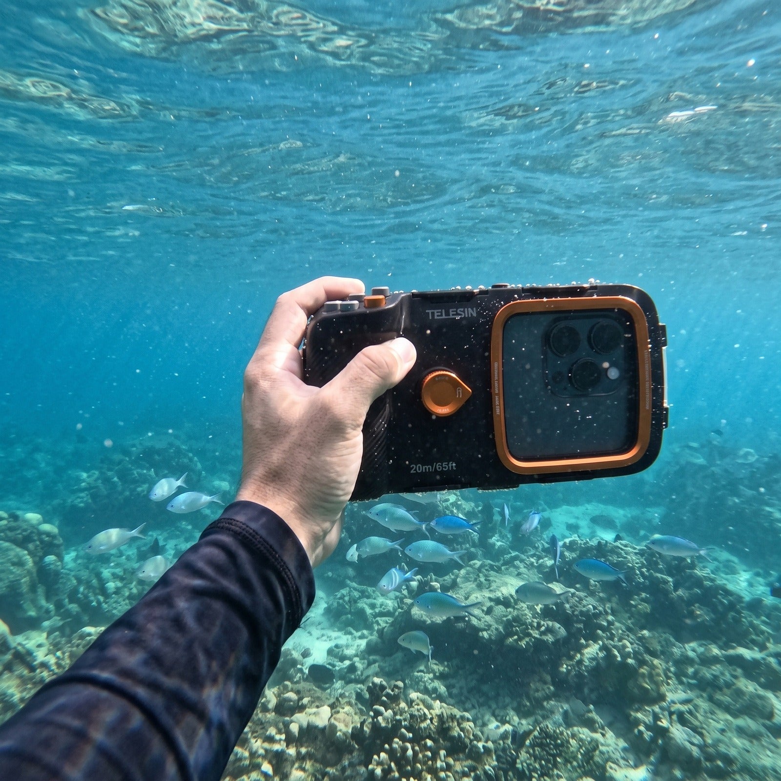 Hands holding the Tideglass housing above an underwater reef